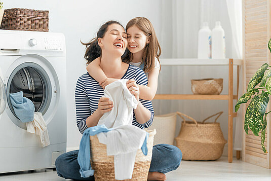 Junge Mutter und kleine Helferin haben Spaß beim Waschen zu Hause.